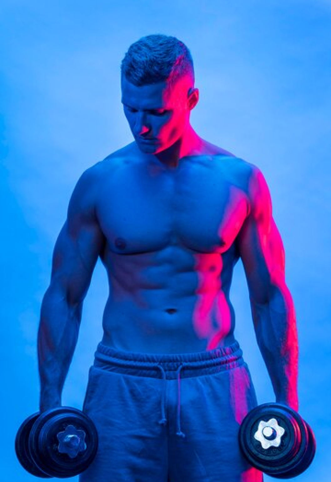 Спортивный мужчина в спортивных штанах голым торсом держит в руках гантели